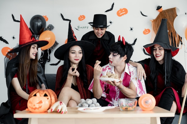 Grupo de jóvenes asiáticos en traje de bruja, mago, infierno celebrar fiesta en la sala para el tema de Halloween en casa. Pandilla adolescente tailandés con celebrar la fiesta de Halloween con una sonrisa. Concepto de fiesta de Halloween en casa.