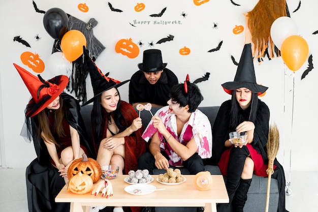 Grupo de jóvenes asiáticos en traje de bruja, mago, infierno celebrar fiesta en la sala para el tema de Halloween en casa. Pandilla adolescente tailandés con celebrar la fiesta de Halloween con una sonrisa. Concepto de fiesta de Halloween en casa.