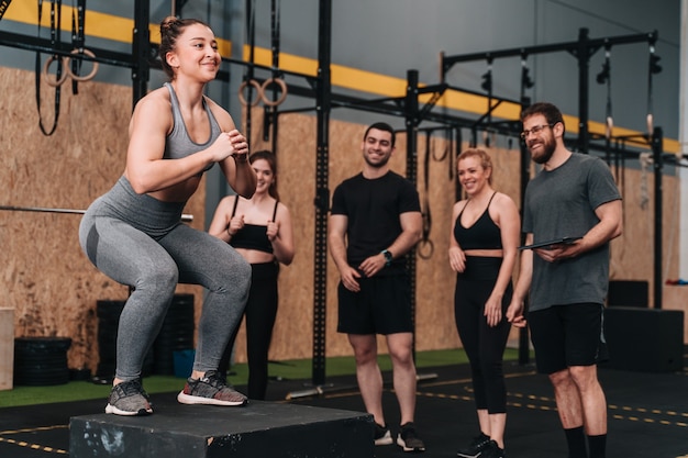 Foto un grupo de jóvenes atletas en un gimnasio de crossfit haciendo una variedad de rutinas de ejercicio mientras el entrenador y otros miembros del grupo los animan