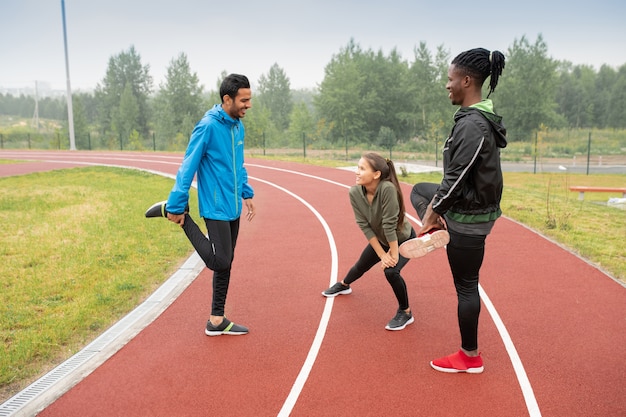 Grupo de jóvenes atletas interculturales haciendo ejercicios de wam-up en pistas de carreras mientras se preparan para el maratón en el estadio