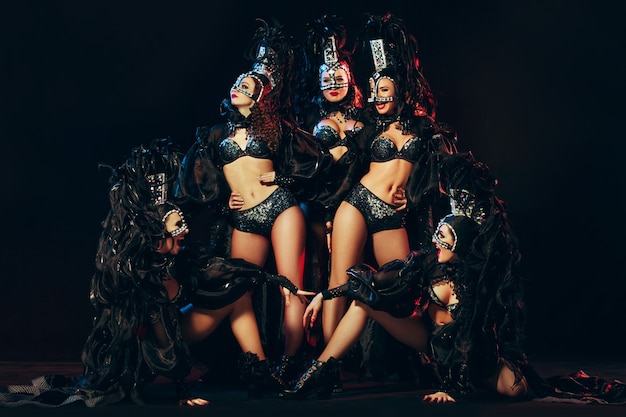 El grupo de jóvenes bailarinas hermosas sonrientes felices con vestidos de carnaval posando sobre fondo negro de estudio