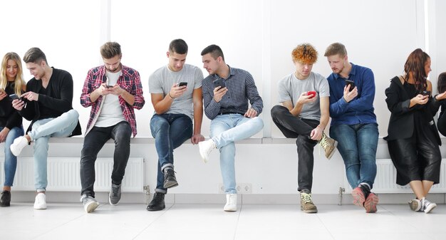 Grupo de jóvenes casuales con teléfonos inteligentes sentados en una foto de fila con copyspace