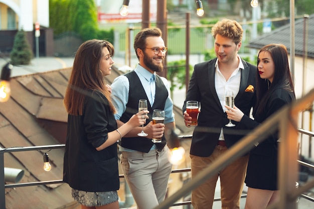 Grupo de jóvenes caucásicos celebrando, lucir feliz, tener una fiesta corporativa en la oficina o en el bar