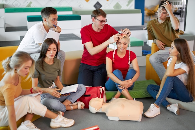 Grupo de jóvenes caucásicos practican el tratamiento de un paciente con vendajes