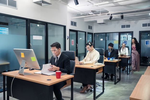 Grupo de jóvenes colegas asiáticos que trabajan con un portátil en un escritorio en la oficina moderna