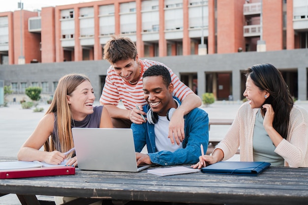 Grupo de jóvenes compañeros estudiando juntos y preparando un examen usando una computadora portátil navegando por Internet