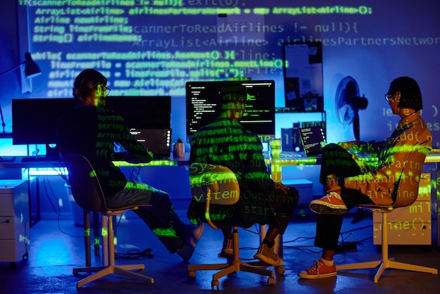 Grupo de jóvenes compañeros de trabajo interculturales sentados en escritorios frente a las computadoras