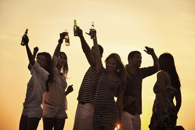 Grupo de jóvenes disfrutan de la fiesta de verano en la playa en la hermosa puesta de sol