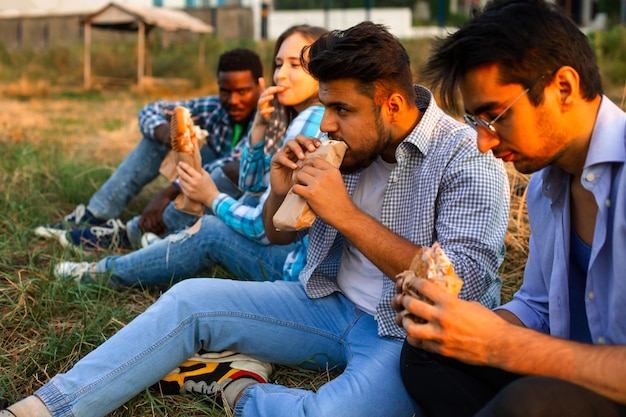 El grupo de jóvenes diversos comiendo comida rápida en la naturaleza.