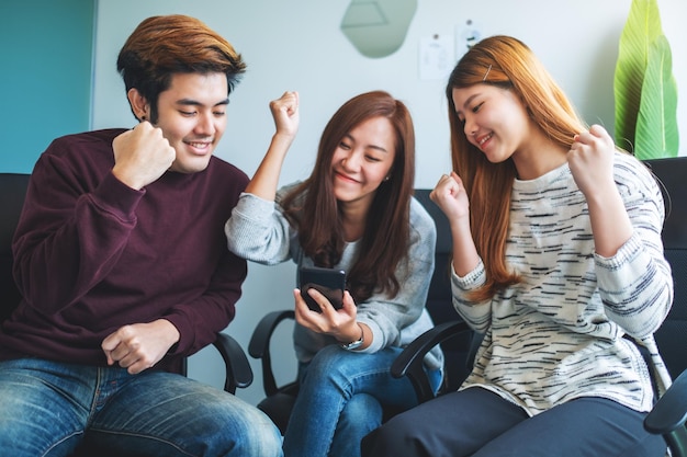 Un grupo de jóvenes divirtiéndose y celebrando mientras miran juntos por teléfono móvil