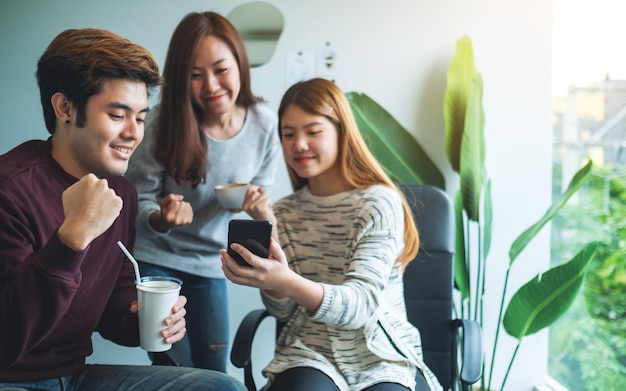 Un grupo de jóvenes divirtiéndose y celebrando mientras miran juntos por teléfono móvil