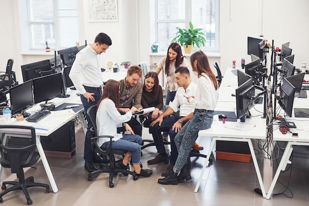 Grupo de jóvenes empleados hablando y trabajando en un nuevo proyecto en la oficina.