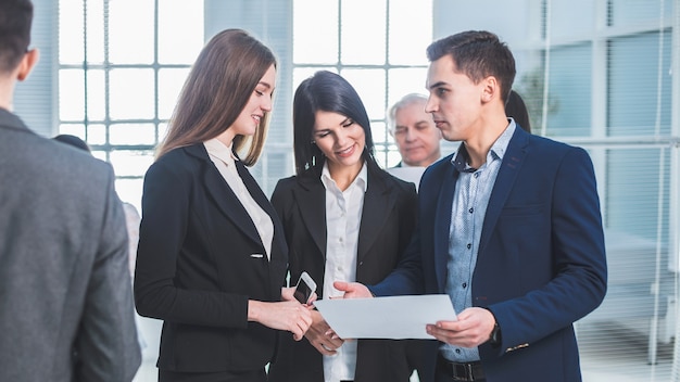 Grupo de jóvenes empleados de pie en el vestíbulo de la oficina durante una pausa laboral. días laborables de oficina