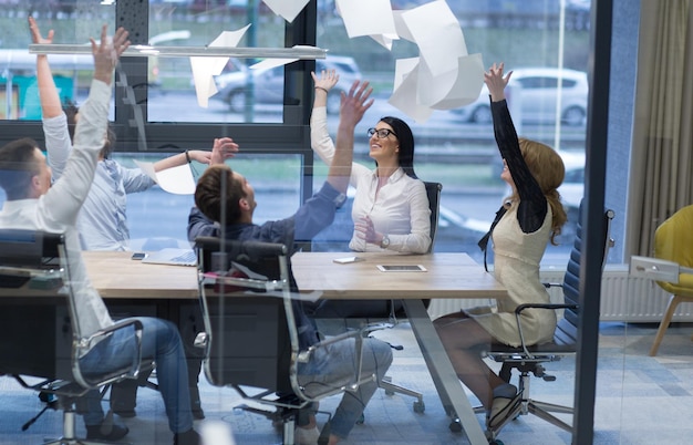 Grupo de jóvenes empresarios arrojando documentos y luciendo felices mientras celebran el éxito en sus lugares de trabajo en la oficina de inicio