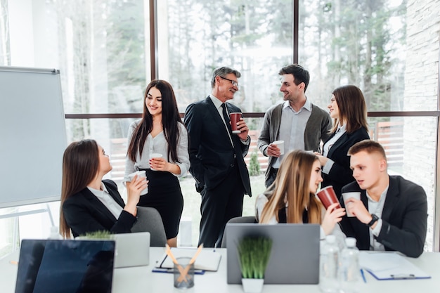 Grupo de jóvenes empresarios en descanso en el cargo. Equipo de negocios exitoso hablando sobre coffee break. Jóvenes colegas sonrientes en descanso bebiendo café charlando en la oficina moderna. Estilo de vida corporativo