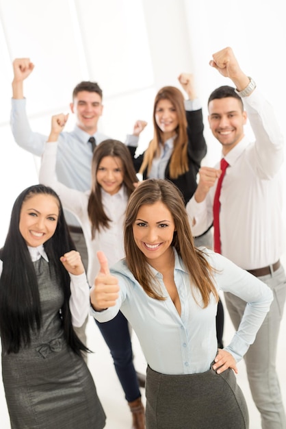 Grupo de jóvenes empresarios exitosos de pie con los pulgares hacia arriba y mirando la cámara.