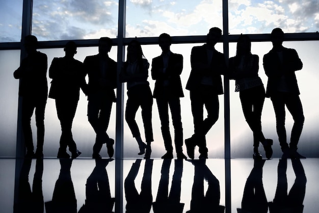 Foto grupo de jóvenes empresarios felices parados cerca de una gran ventana de oficina