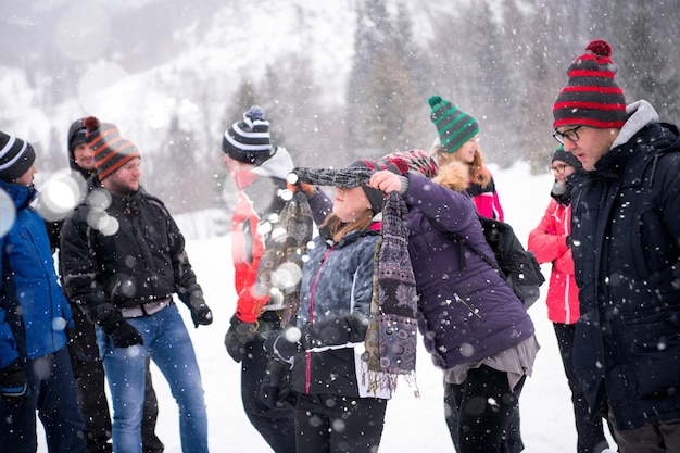 grupo de jóvenes empresarios felices que tienen una competencia de juegos con los ojos vendados mientras disfrutan de un día de invierno nevado con copos de nieve a su alrededor durante un equipo en el bosque de montaña