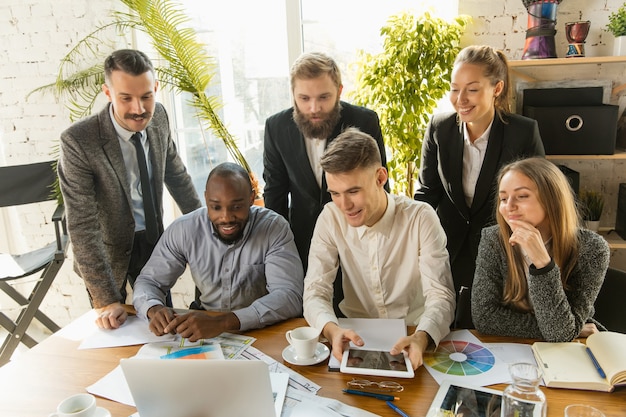 Grupo de jóvenes empresarios que tienen una reunión. Grupo diverso de compañeros de trabajo discuten nuevas decisiones, planes futuros y estrategias. Reunión creativa y lugar de trabajo, negocios, finanzas, trabajo en equipo.