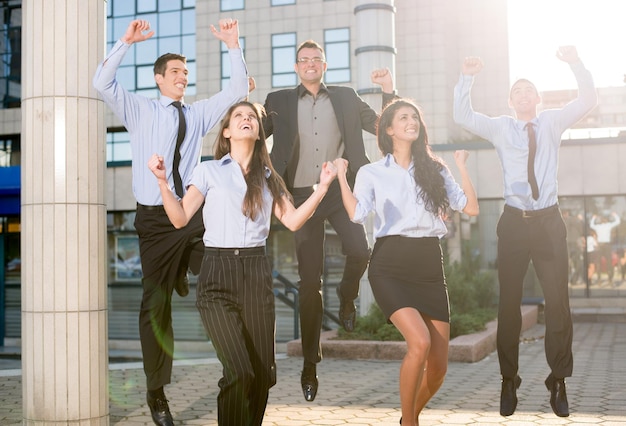 Grupo de jóvenes empresarios saltando frente a la empresa celebrando un trabajo exitoso.