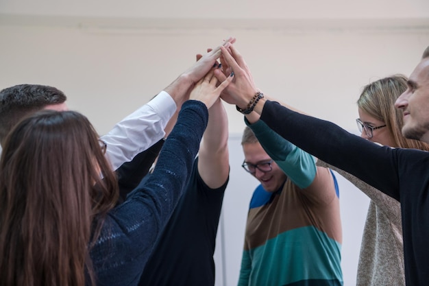 Grupo de jóvenes estudiantes en el aula de electrónica celebrando un proyecto terminado con éxito manteniendo sus manos juntas, concepto de educación y tecnología