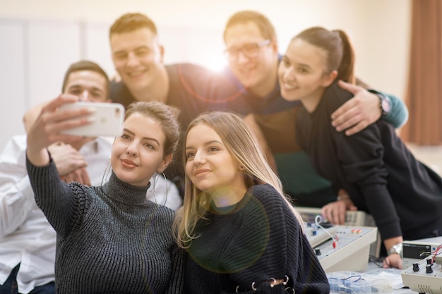 grupo de jóvenes estudiantes felices haciendo una foto selfie usando un teléfono inteligente después de un día exitoso en el aula de electrónica