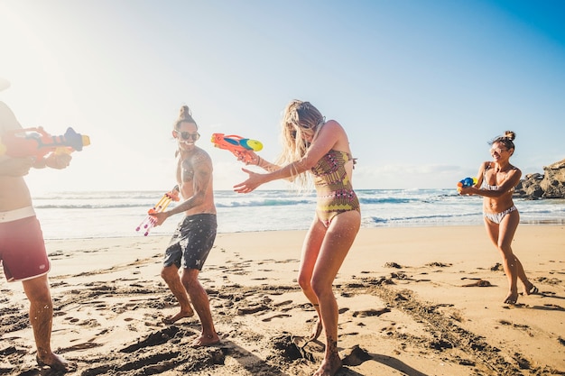 Grupo de jóvenes felices y alegres que se divierten juntos en friendshp con una batalla de pistolas de agua en la playa durante las vacaciones de verano