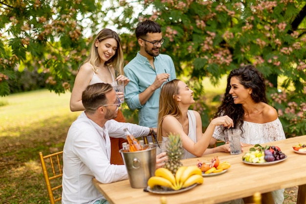 Grupo de jóvenes felices animando con limonada fresca y comiendo frutas en el jardín