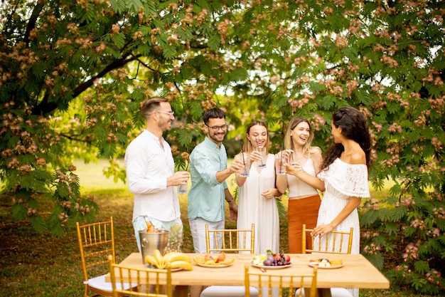 Grupo de jóvenes felices animando con limonada fresca y comiendo frutas en el jardín