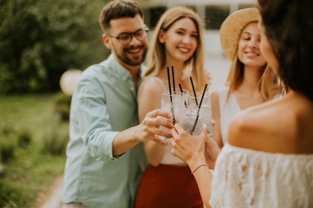 Grupo de jóvenes felices animando con limonada fresca en el jardín