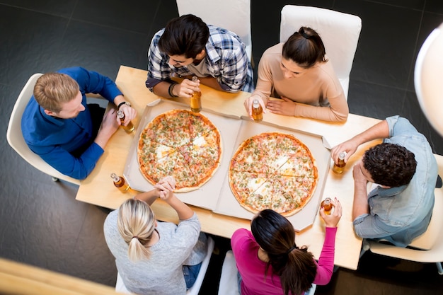 Grupo de jóvenes felices comiendo pizza y bebiendo sidra en el interior moderno