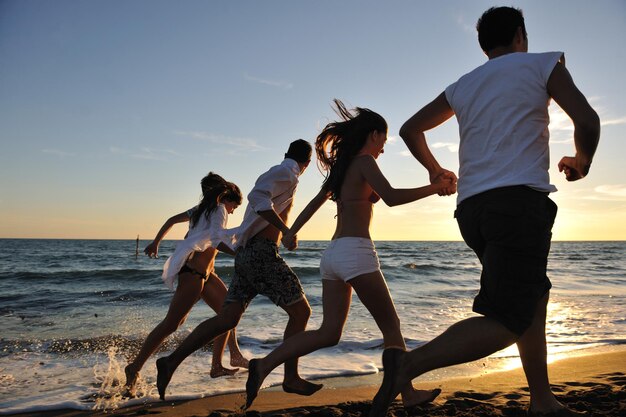 el grupo de jóvenes felices se divierten corriendo y saltando en beacz al atardecer