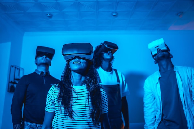 Grupo de jóvenes con gafas vr en un juego de realidad virtual en un concepto futurista de luz azul o tecnología científica jugando juntos en casa