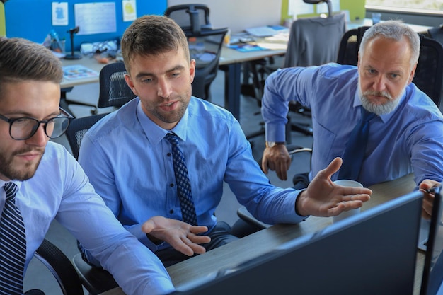 Grupo de jóvenes hombres de negocios en ropa formal trabajando usando computadoras mientras están sentados en la oficina