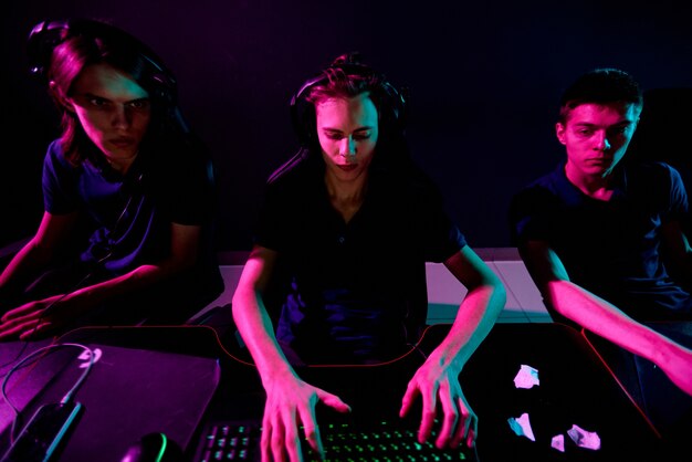 Grupo de jóvenes jugadores de videojuegos ciberdeportivos contemporáneos con auriculares que desarrollan un nuevo juego mientras uno de ellos escribe en el teclado