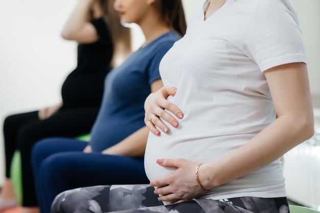 Un grupo de jóvenes madres embarazadas se dedican a Pilates y deportes de pelota en un gimnasio. Primer plano del vientre