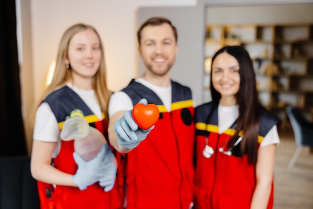 Un grupo de jóvenes médicos uniformados se paran en medio del salón de clases y sonríen después de una lección de primeros auxilios Un hombre sostiene un corazón rojo en sus manos Concepto de asistencia