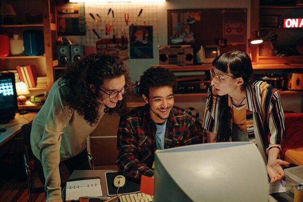 Grupo de jóvenes mirando el monitor de la computadora y discutiendo un nuevo proyecto