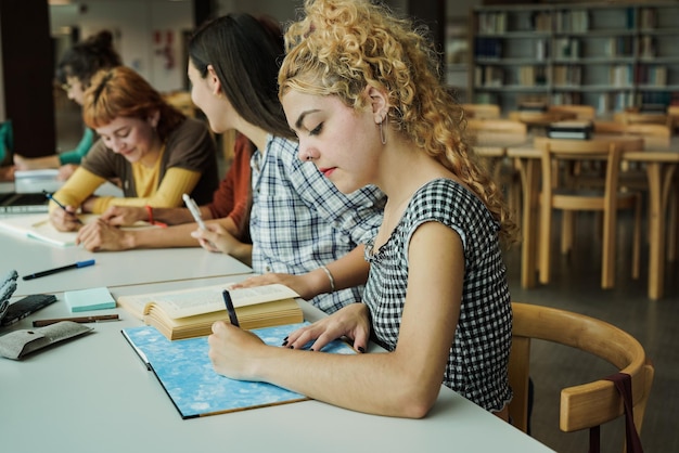 Grupo de jóvenes mujeres diversas que estudian dentro de la biblioteca en la universidad