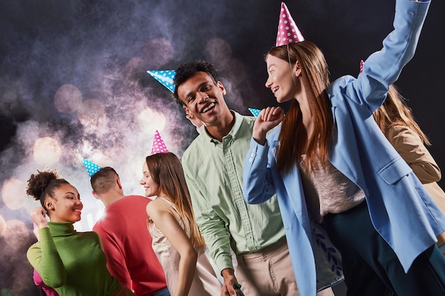 Foto grupo de jóvenes multirraciales felices con sombreros de cumpleaños riendo y divirtiéndose