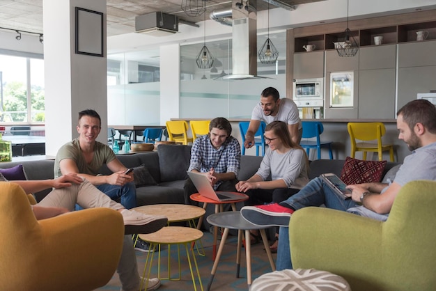 Foto el grupo de jóvenes en la oficina moderna tiene una reunión de equipo y una lluvia de ideas mientras trabaja en una computadora portátil y toma café