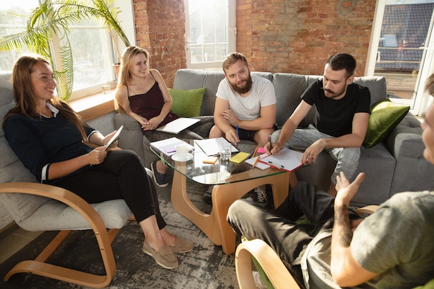 Foto grupo de jóvenes oficinistas caucásicos reunidos para discutir nuevas ideas. reunión creativa. trabajo en equipo y lluvia de ideas. hombres y mujeres se reúnen en la oficina para planificar su trabajo futuro. concepto de negocio.