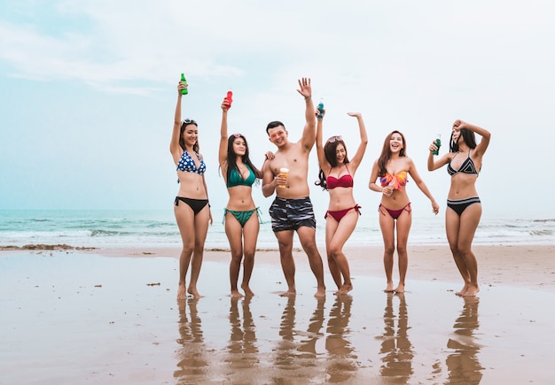 Foto grupo de jóvenes que se divierten bebiendo y bailando en la playa en vacaciones de verano