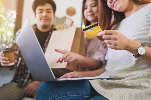 Grupo de jóvenes que usan laptop y tarjeta de crédito para comprar juntos en línea