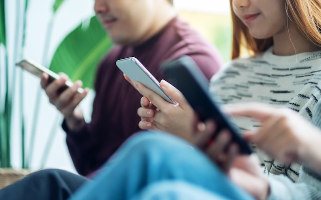 Grupo de jóvenes que usan y miran el teléfono móvil mientras están sentados juntos