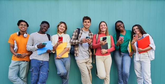Grupo de jóvenes de raza mixta que usan teléfonos móviles estudiantes al aire libre aislados en fondo azul