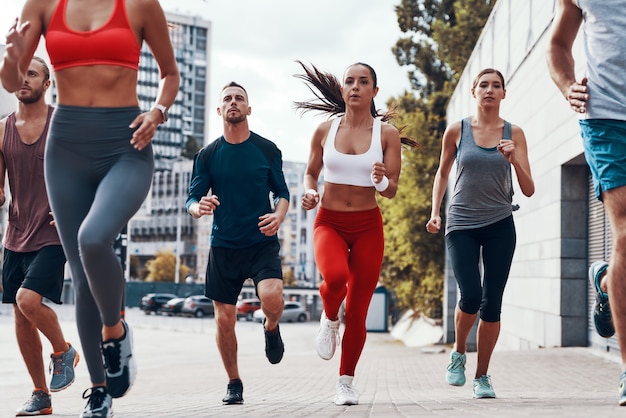 Grupo de jóvenes en ropa deportiva para correr mientras hace ejercicio en la acera al aire libre