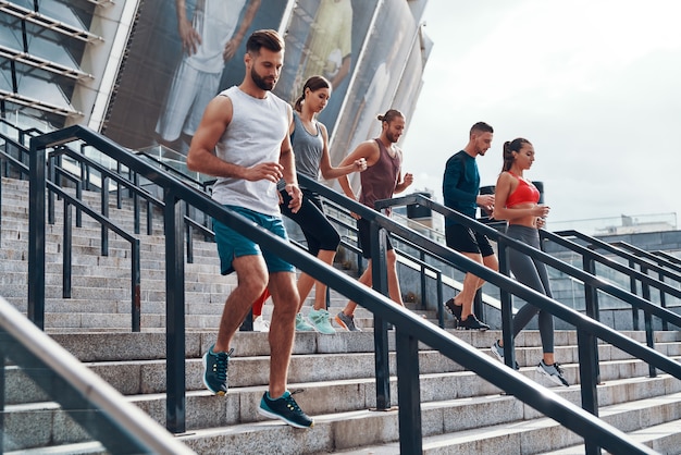 Grupo de jóvenes en ropa deportiva para correr mientras hace ejercicio en las escaleras al aire libre