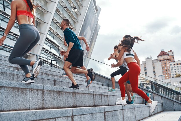 Grupo de jóvenes en ropa deportiva para correr mientras hace ejercicio en las escaleras al aire libre