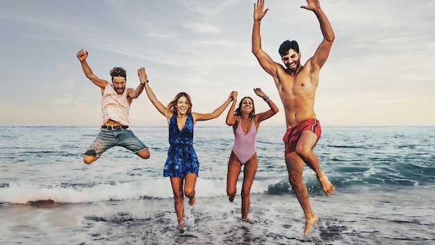 Grupo de jóvenes saltando por el mar amigos divirtiéndose corriendo por las olas gen z personas concepto de estilo de vida de verano